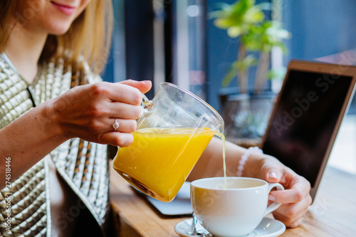 Positive thoughtful female distance worker in cafe drinking sea buckthorn tea. Rest in the weekend in your favorite cafe, mature businerss woman traveler sits in cafe over cup of yellow tea pouring it photo