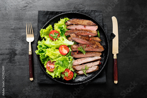 Sliced grilled beef steak and green salad leaves on black plate.Top wiev.