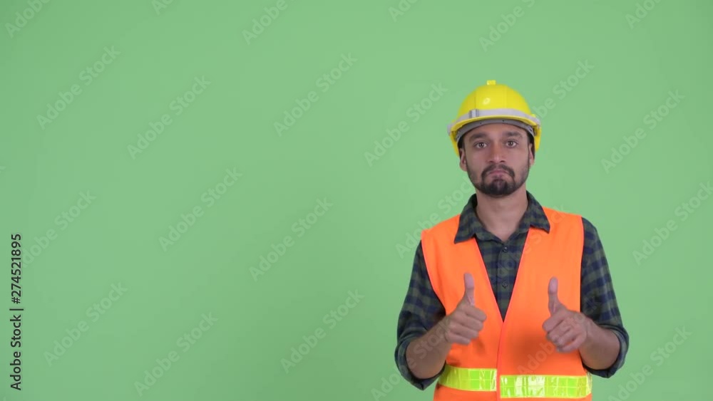 Young bearded Persian man construction worker thinking while pointing up Young bearded Persian man construction worker thinking while pointing up