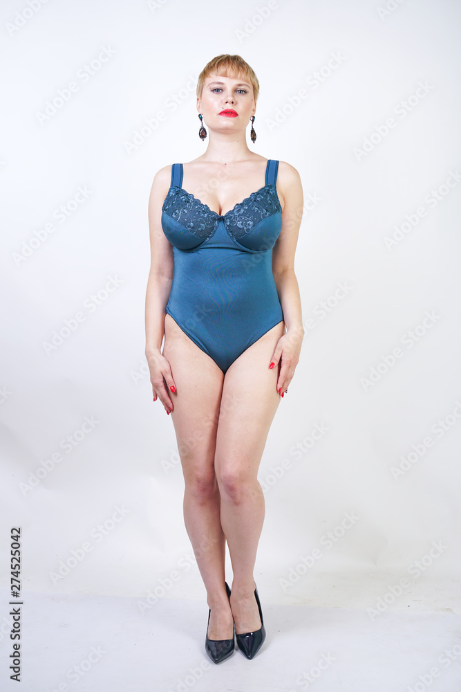 pretty plus size woman with short hair and chubby curvy body wearing retro bodysuit underwear and posing on white studio background alone. beautiful plump girl standing in pin up vintage lingerie.