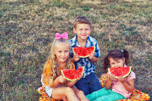 Children with watermelon in nature . A group of children on a picnic with a ripe watermelon