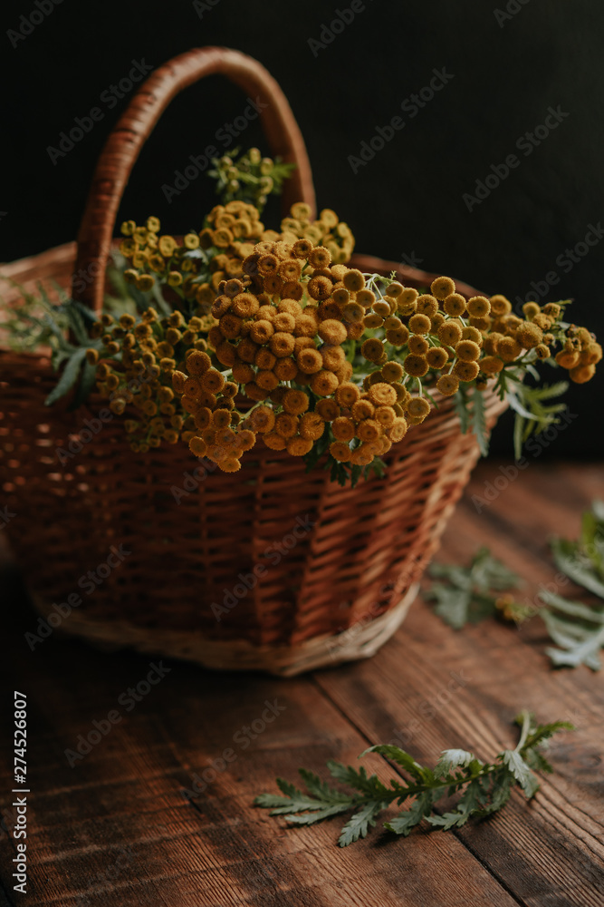 Autumn composition with yellow tansy flowers in a wicker basket on a wooden background Autumn composition with yellow tansy flowers in a wicker basket on a wooden background