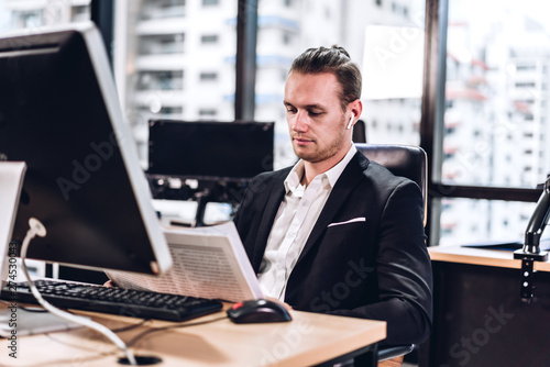 Confident young handsome businessman reading newspaper and working with computer in modern office © Art_Photo