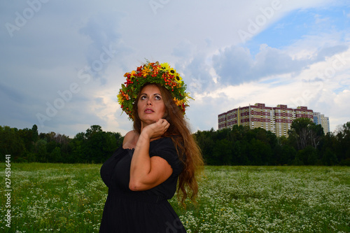 A young woman with a wreath on her head standing in a green field.