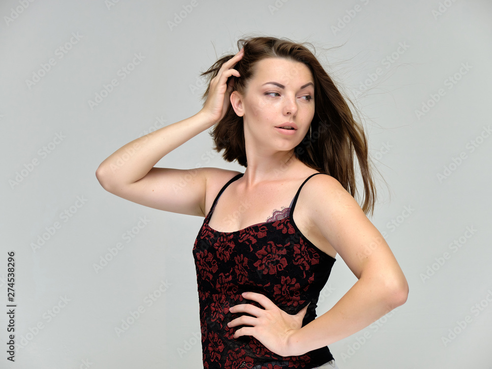 Fototapeta premium Closeup portrait of pretty girl, brunette woman 30 years old on a light gray background with beautiful dark hair and excellent skin of the face and body. She shows emotions, smiles, wonders.