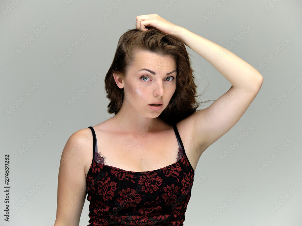 Fototapeta premium Closeup portrait of pretty girl, brunette woman 30 years old on a light gray background with beautiful dark hair and excellent skin of the face and body. She shows emotions, smiles, wonders.