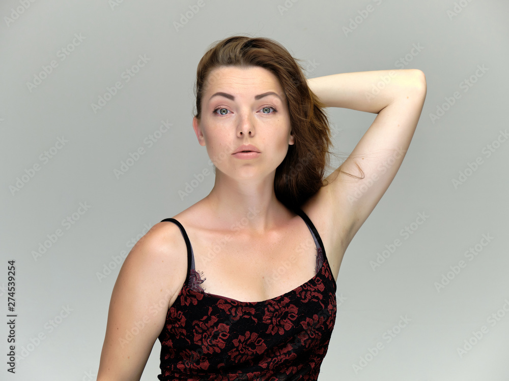 Fototapeta premium Closeup portrait of pretty girl, brunette woman 30 years old on a light gray background with beautiful dark hair and excellent skin of the face and body. She shows emotions, smiles, wonders.