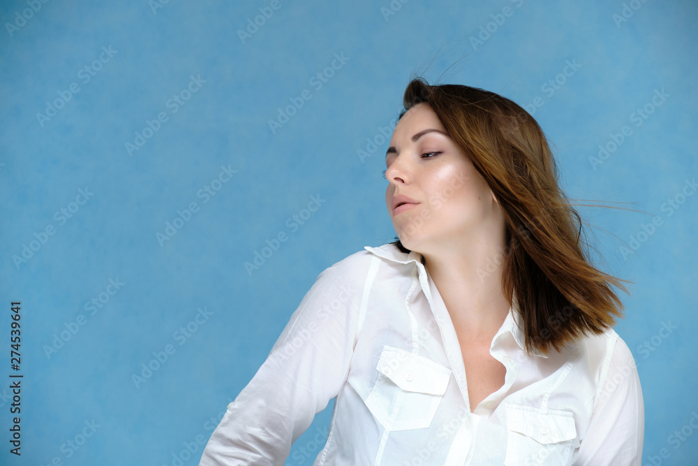 A close-up portrait of a pretty girl, a brunette woman, 30 years old, against a blue background in a white shirt with dark hair and excellent skin. She shows emotions, smiles, wonders. A close-up portrait of a pretty girl, a brunette woman, 30 years old, against a blue background in a white shirt with dark hair and excellent skin. She shows emotions, smiles, wonders.