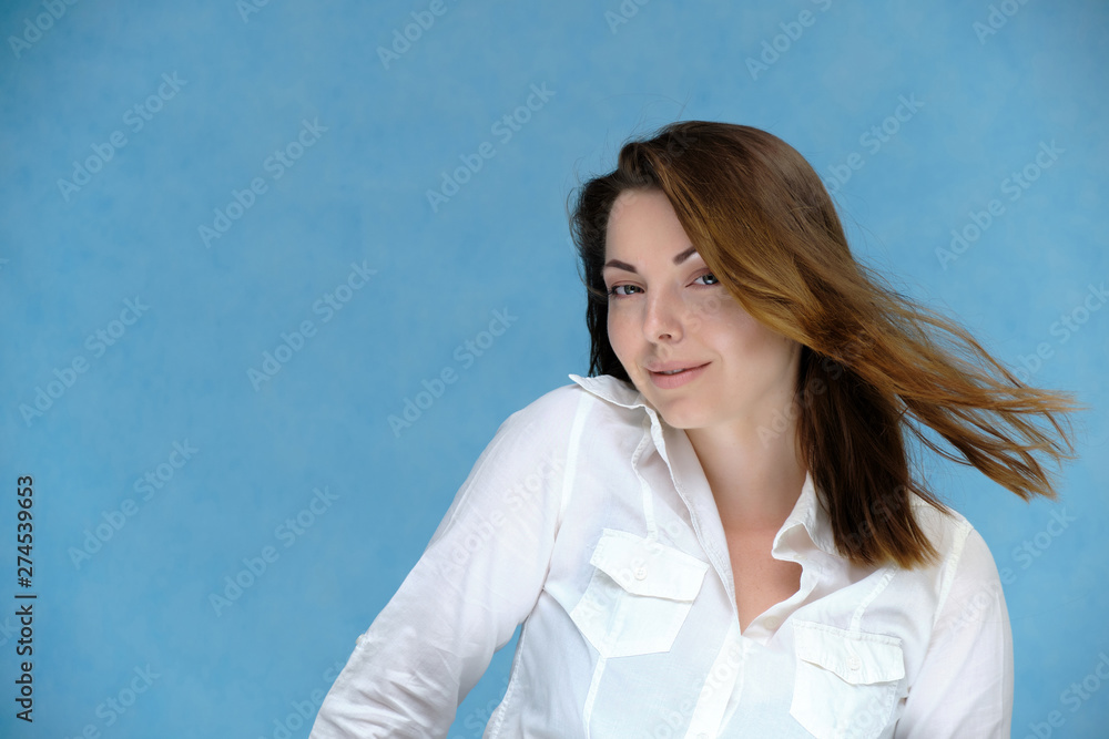 A close-up portrait of a pretty girl, a brunette woman, 30 years old, against a blue background in a white shirt with dark hair and excellent skin. She shows emotions, smiles, wonders. A close-up portrait of a pretty girl, a brunette woman, 30 years old, against a blue background in a white shirt with dark hair and excellent skin. She shows emotions, smiles, wonders.