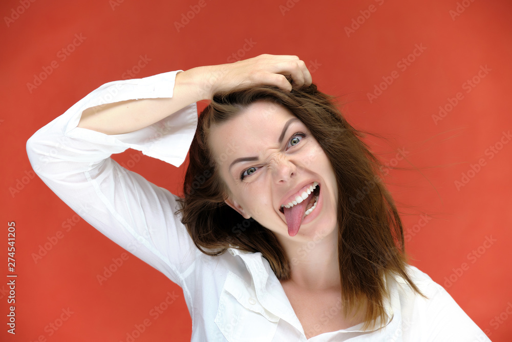 Naklejka premium A close-up portrait of a pretty girl, a brunette woman of 30 years old on a red background in a white shirt with flowing dark hair and excellent skin. She shows emotions, smiles, wonders.