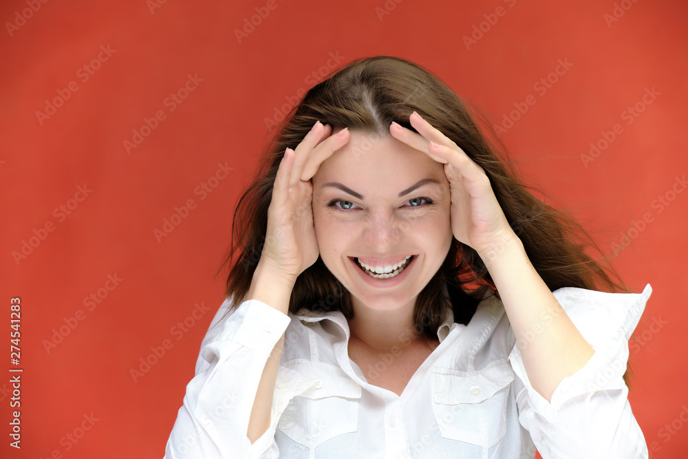 A close-up portrait of a pretty girl, a brunette woman of 30 years old on a red background in a white shirt with flowing dark hair and excellent skin. She shows emotions, smiles, wonders. A close-up portrait of a pretty girl, a brunette woman of 30 years old on a red background in a white shirt with flowing dark hair and excellent skin. She shows emotions, smiles, wonders.
