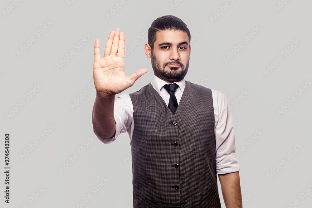 Give me five or stop! Portrait of handsome bearded brunette man in white shirt and waistcoat standing, looking at camera and showing his hand. indoor studio shot isolated on gray background. Give me five or stop! Portrait of handsome bearded brunette man in white shirt and waistcoat standing, looking at camera and showing his hand. indoor studio shot isolated on gray background.