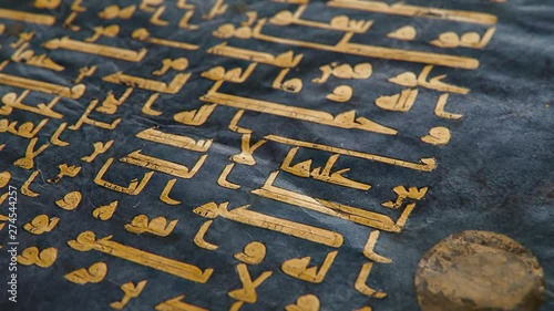 The Blue Qur'an manuscript in Kufic calligraphy written in gold and silver on indigo-dyed parchment, shallow depth of field close-up slow tilt up CGI shot.
