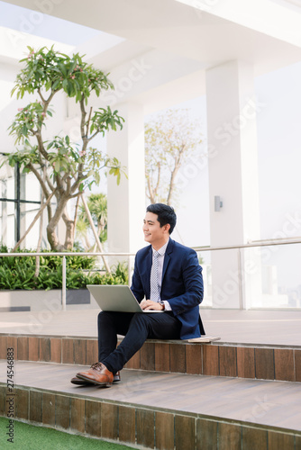 Happy young businessman using laptop outside office building