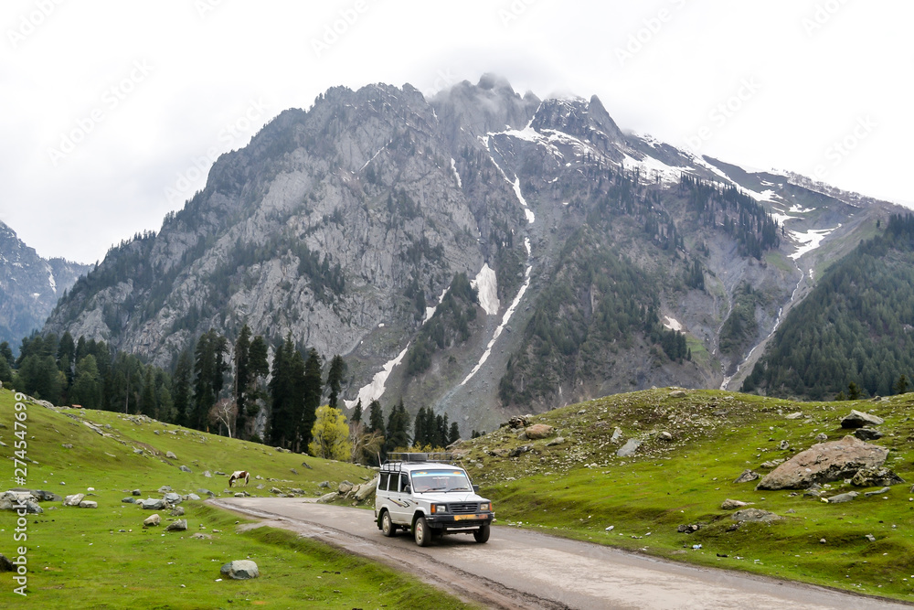 Off-road SUV driving on the rock mountain road in Kashmir Betaab valley (Paradise on Earth) Srinagar, Pahalgam, Jammu and Kashmir, India. Snow frozen Himalayas glacier mountain at a distance.