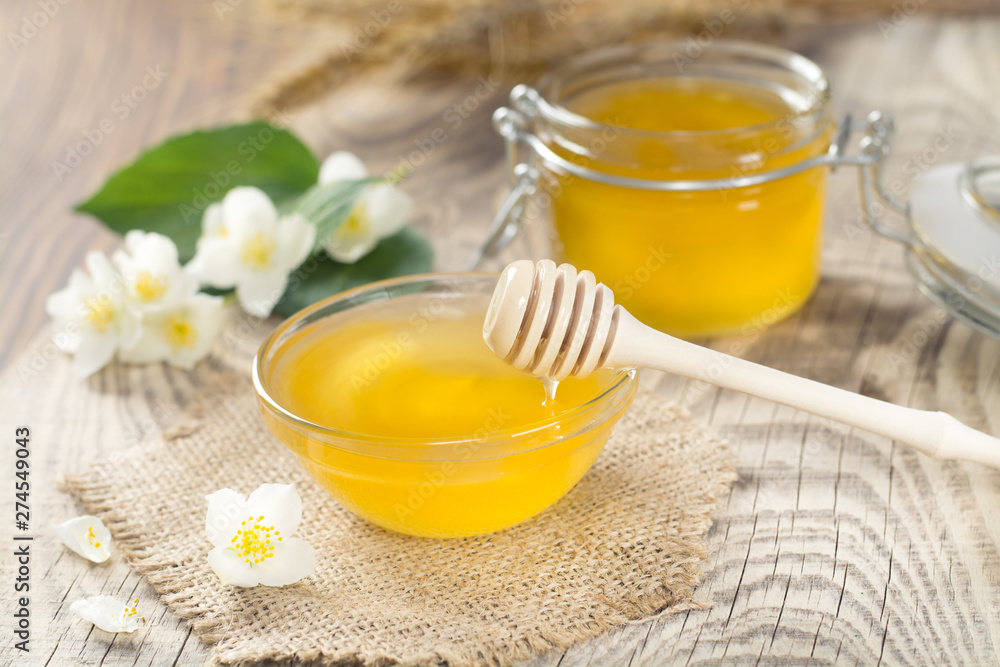 fragrant golden honey in a glass jar with a wooden spoon near a sprig of jasmine flowers fragrant golden honey in a glass jar with a wooden spoon near a sprig of jasmine flowers