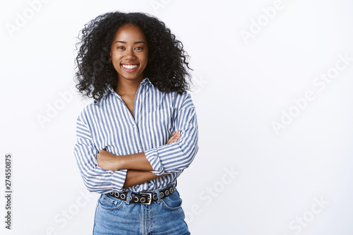 Friendly cheerful attractive african american curly-haired young 25s woman consultant woking talking coworkers smiling pleasant having fun enjoying relaxing company mood, standing hands crossed chest
