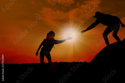 Silhouette of man helping woman to climb on hill against sunset