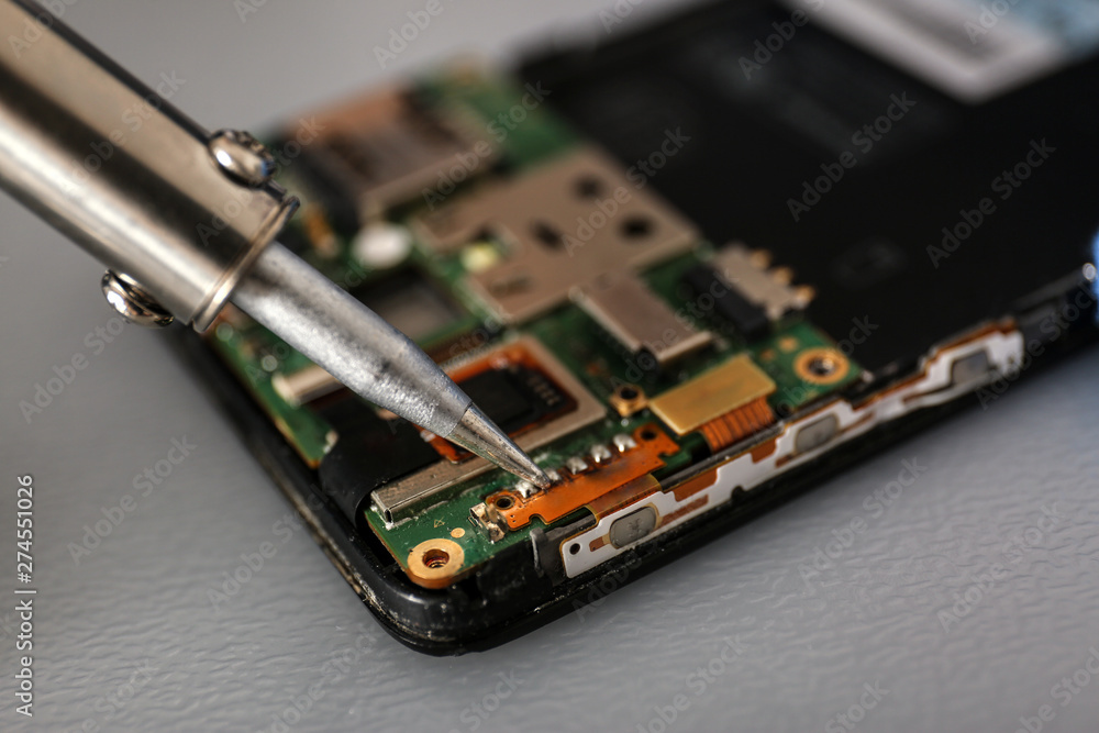 Repairing broken smartphone with soldering iron on table, closeup. Space for text Repairing broken smartphone with soldering iron on table, closeup. Space for text