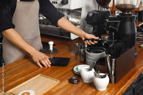 Barista pouring milled coffee from grinding machine into portafilter at bar counter, closeup