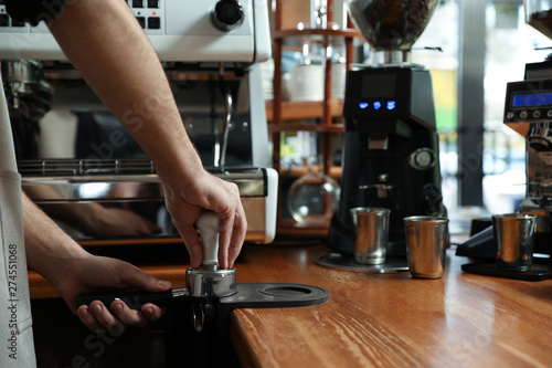 Barista tamping coffee in portafilter at bar counter, closeup. Space for text