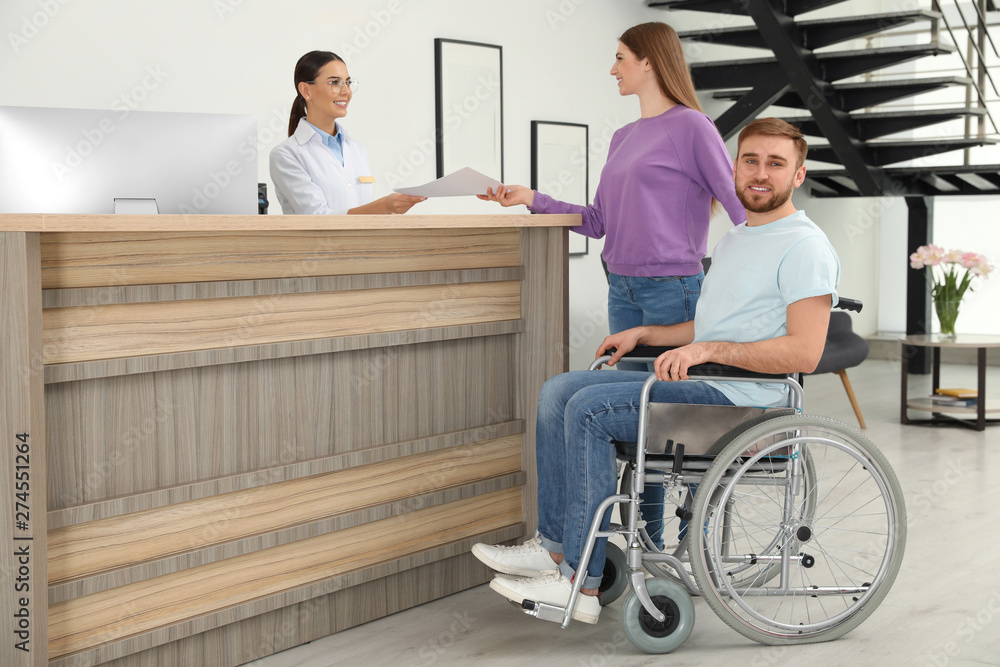 Professional receptionist working with woman and handicapped man at desk in clinic
