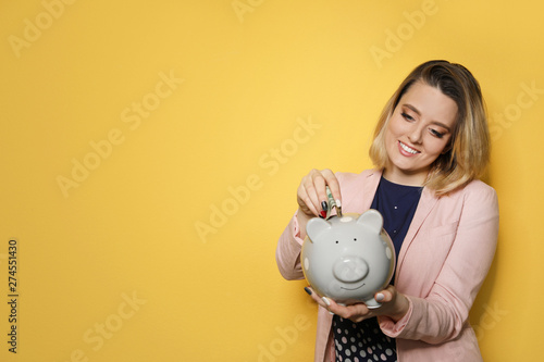 Beautiful businesswoman putting money into piggy bank on color background. Space for text