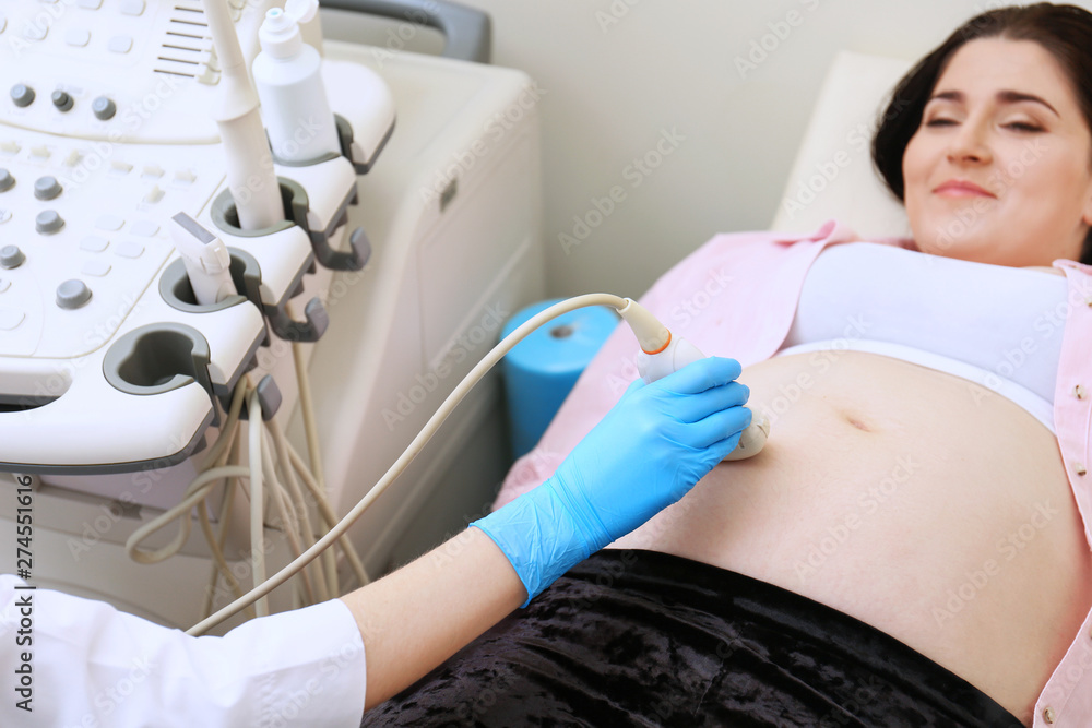 Young pregnant woman undergoing ultrasound scan in clinic Young pregnant woman undergoing ultrasound scan in clinic