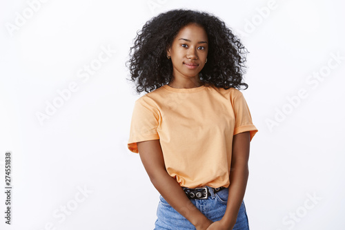 Attractive friendly-looking polite shy african-american female student smiling lovely holding palms together showing parents grades acting angel, standing orange t-shirt jeans white background photo