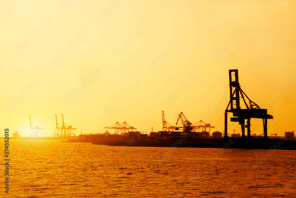 Silhouette of container and gantry crane at Osaka port are loading on evening with sunset glow background.