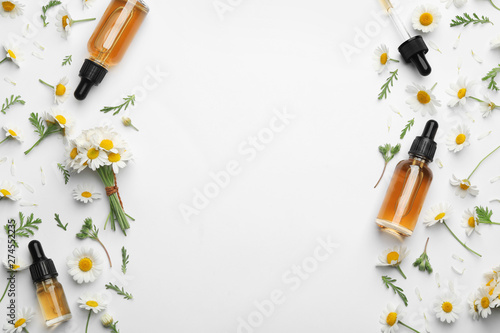 Chamomile flowers and cosmetic bottles of essential oil on white background, top view. Space for text
