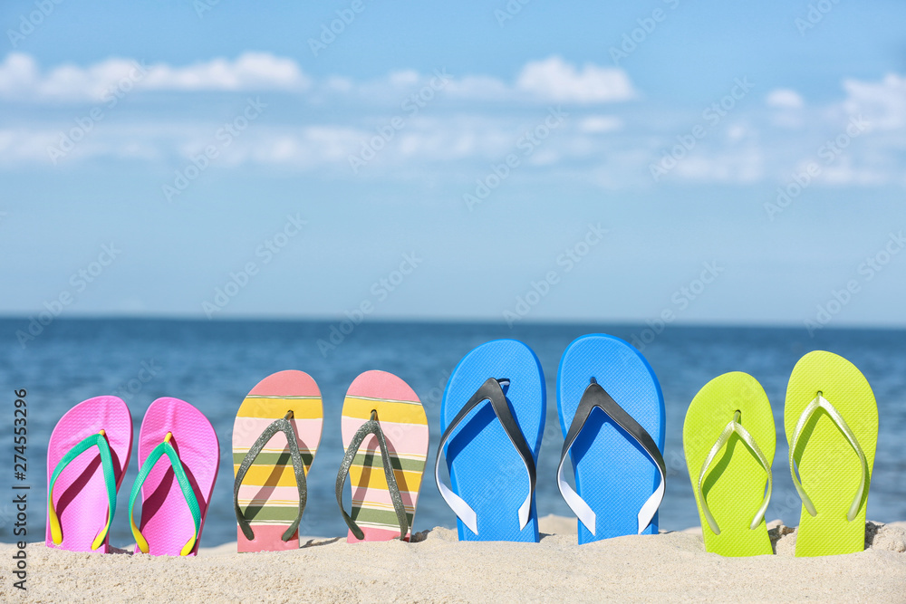 Obraz premium Composition with bright flip flops on sand near sea in summer. Beach accessories