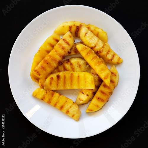 Grilled pineapple wedges on a white plate on a black surface. Summer food. Close-up.