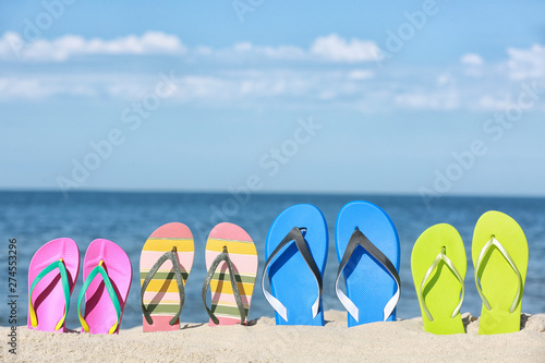 Composition with bright flip flops on sand near sea in summer. Beach accessories
