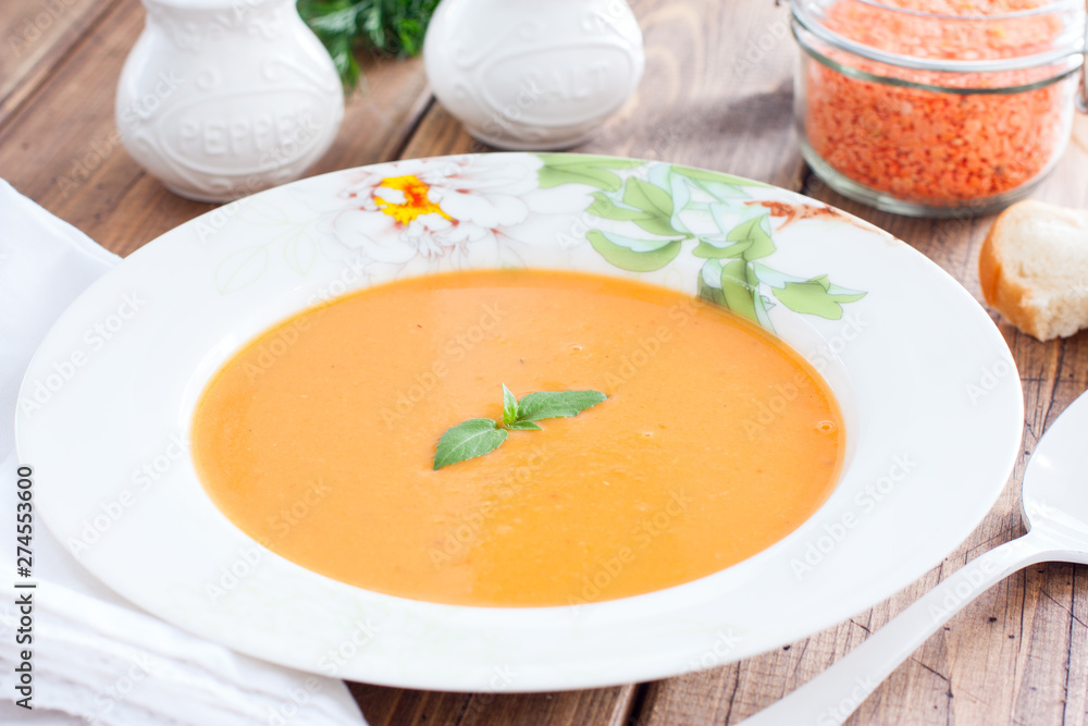 Red lentil cream soup in a white plate on a wooden table, horizontal Red lentil cream soup in a white plate on a wooden table, horizontal