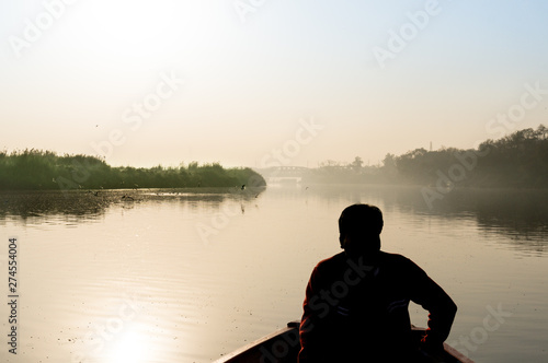 silhouette of boatsman rowing out into the yamuna ganga river in the morning
