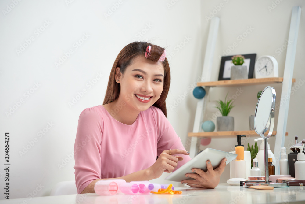 Happy asian woman wearing hair curlers using tablet at home Happy asian woman wearing hair curlers using tablet at home