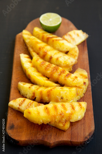 Grilled pineapple wedges on a rustic wooden board on a black background, low angle view. Summer food. Close-up.