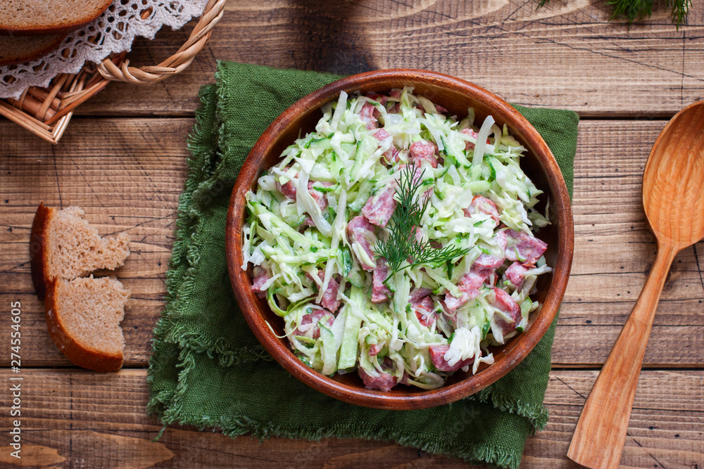 Salad with fresh cabbage and smoked sausage in a wooden bowl, top view, horizontal