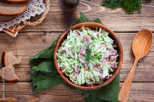 Salad with fresh cabbage and smoked sausage in a wooden bowl, top view, horizontal