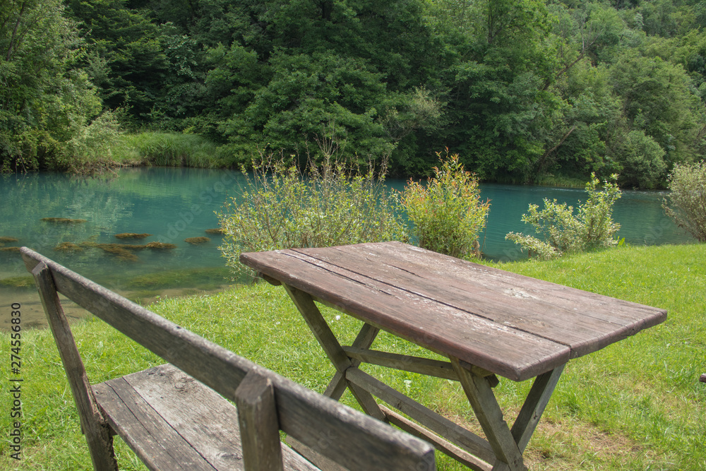 Home made wooden bench and table next to very scenic and green river bank