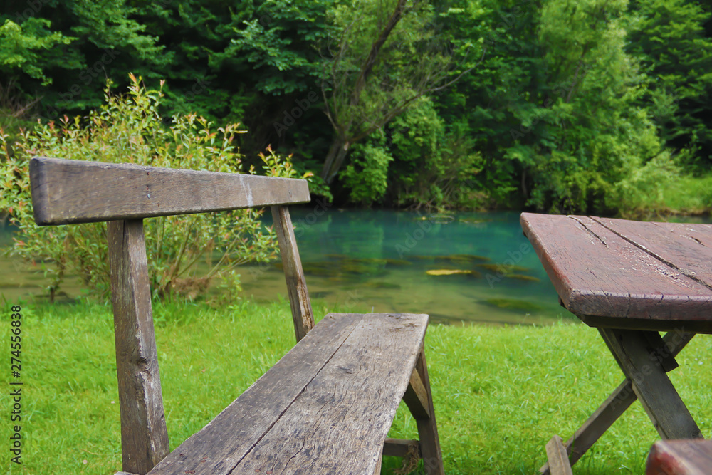 Home made wooden bench and table next to very scenic and green river bank