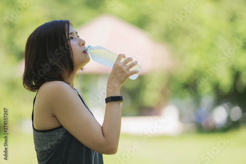 Pretty young woman drinking water during exercise in the park on a summer day