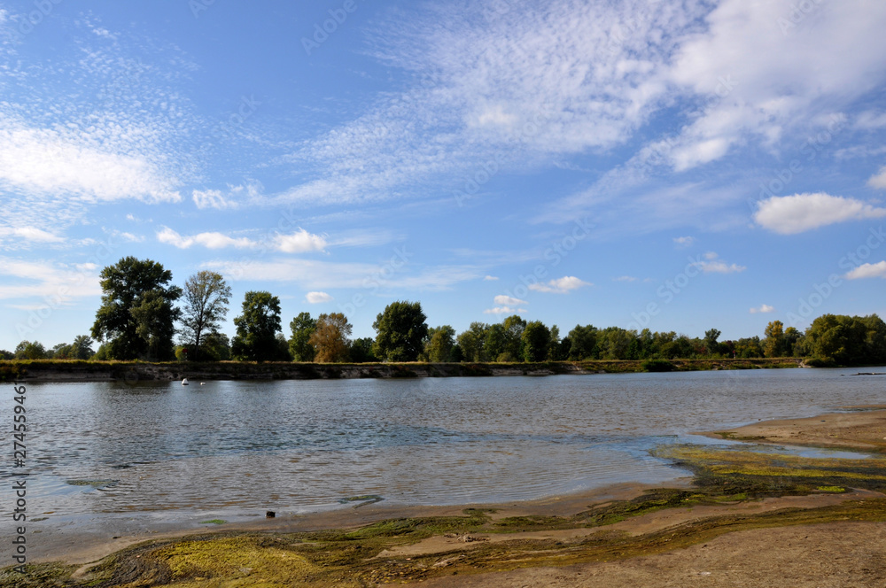 Obraz premium Wide blue river is slow flowing. Summer. Sunny weather and white sand. green trees far away