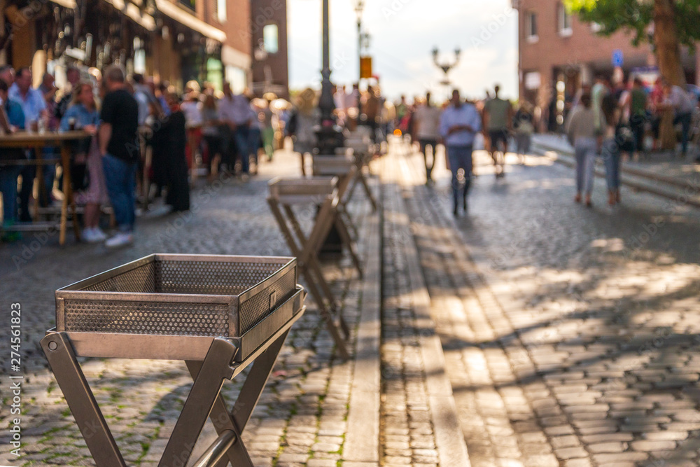 Outdoor sunny selected focus view of empty metal trays for glass of beer alongside the walking street, and blur background of people stand, hang out and drink beer in old town Düsseldorf, Germany. Outdoor sunny selected focus view of empty metal trays for glass of beer alongside the walking street, and blur background of people stand, hang out and drink beer in old town Düsseldorf, Germany.