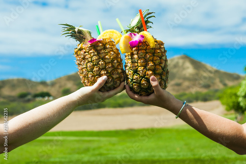 Tropical Pineapple cocktail Pina Colada. Two people making a toast with pineapple shaped glasses and little paper umbrella.