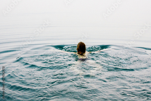 Young beautiful woman is swimming in calm water. The calm water of the lake.
