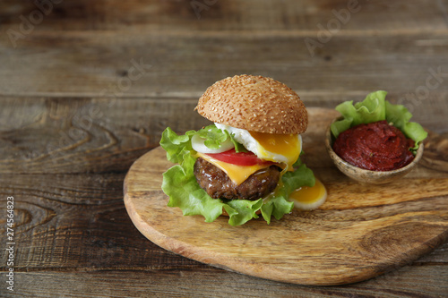 Hamburger with beef cutlet, with vegetables, tomato sauce and fried egg beautifully flowing yolk on a wooden rustic background with copy space for text.