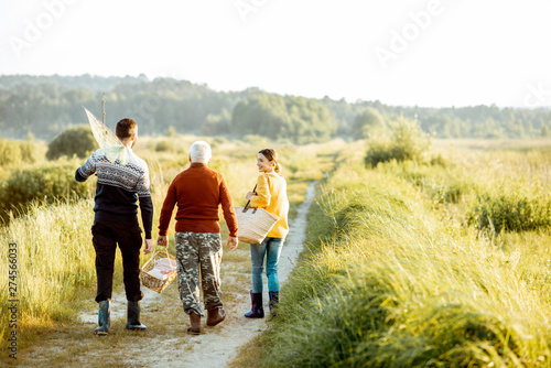 Young man and woman walking on the picnic with senior grandfather dressed in sweaters, spending a good time together on the nature