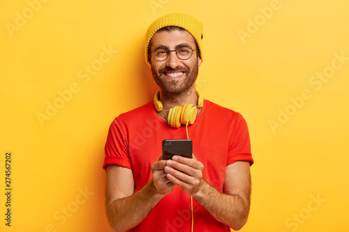 Canvas Print Attractive cheerful guy with bristle, wears bright hat and red t shirt, searches